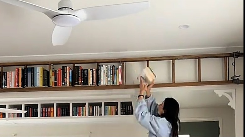 A woman places books on a ladder hung horizontally on the wall