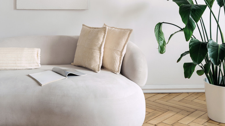 Round sofa with throw pillows and open magazine, next to potted plant