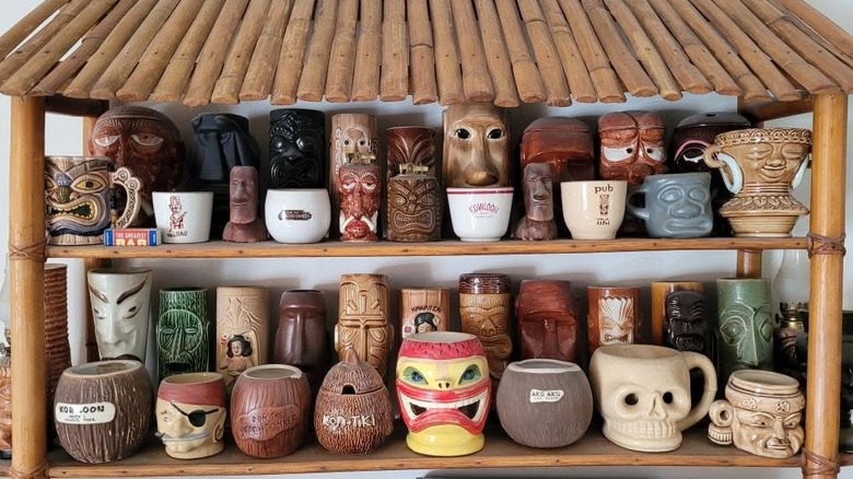 A large mid-century tiki mug collection displayed on a bamboo shelf.