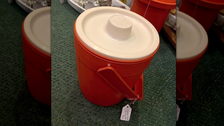 An orange and white vintage Rubbermaid ice bucket sitting on a green carpet.