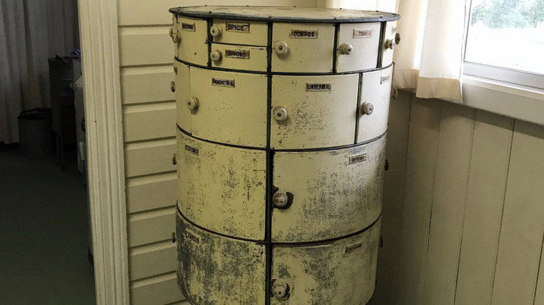 A vintage rotary canister cabinet on display at a historical society museum, each of the compartments labeled with a type of good.