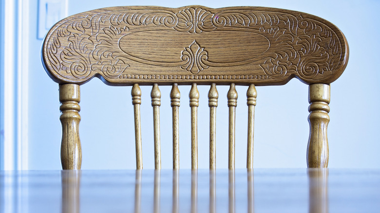 A closeup shows the spindles of a dining chair near a table with a reflective surface