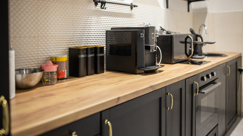 An espresso machine, microwave oven, and tea kettle sitting on a butcher block counterop.