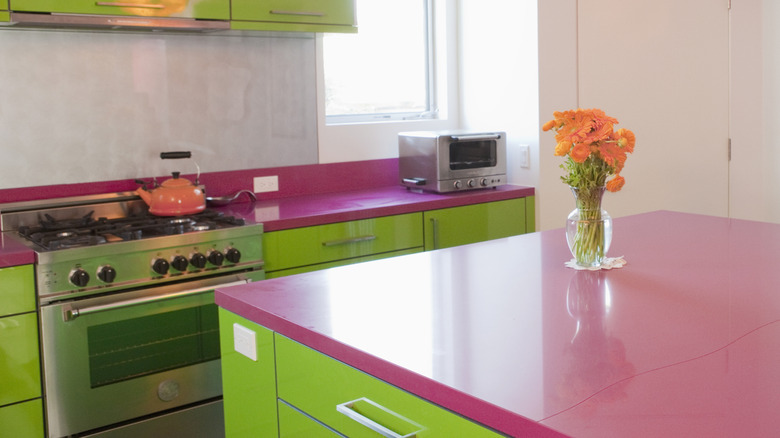 A kitchen with green cabinets and hot pink counter tops.