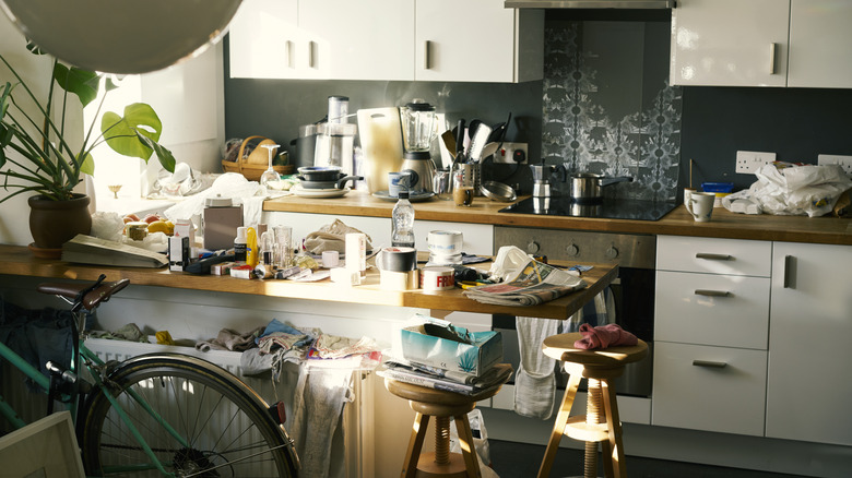 A kitchen with white cabinets and wooden countertops cluttered with random trash and dishes.