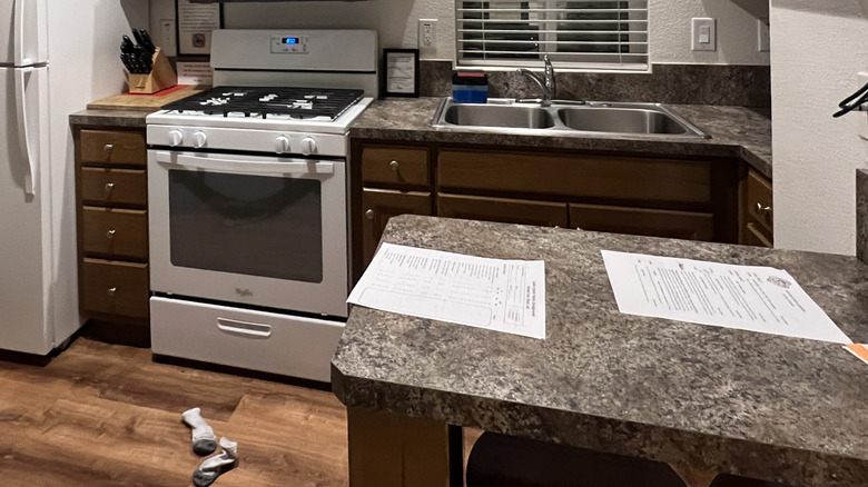 A narrow kitchen with white appliances and peninsula jutting out into room
