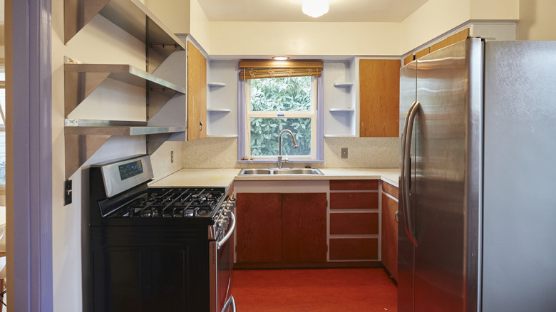 A kitchen with red floors, an oversized fridge, and a black stove-oven combo.
