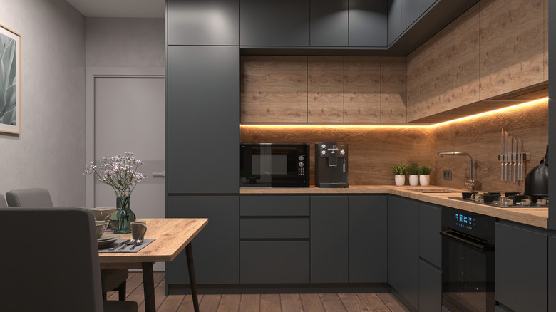 A small corner kitchen in an apartment with no natural light but with undercabinet lighting.