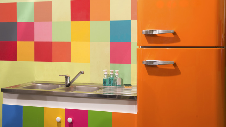 A retro, orange fridge next to a neon color-blocked wall and sink station.