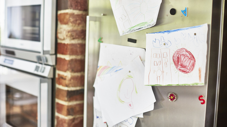 A stainless steel fridge with pieces of children's art work and magnets on the door.