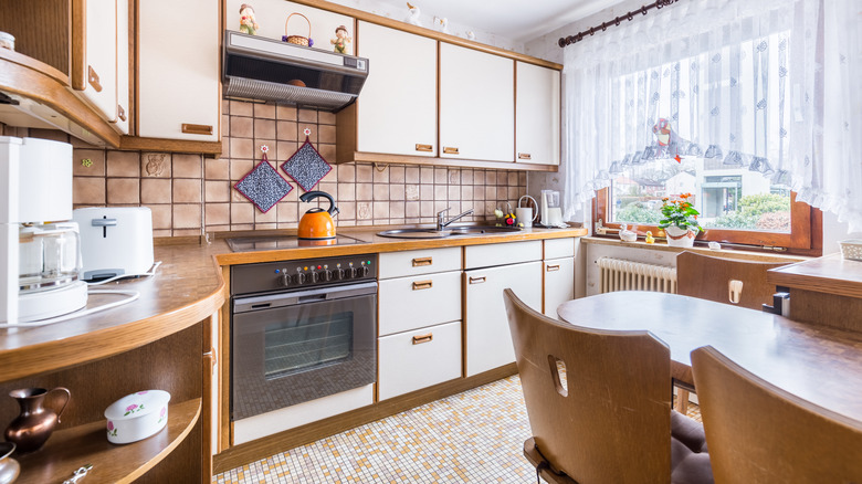 A retro kitchen with small floor tiles and white laminate cabinets.