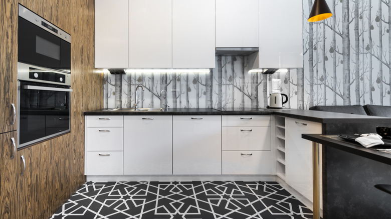 A small kitchen with wooden accent cabinets, a patterned floor, and wallpapered walls.