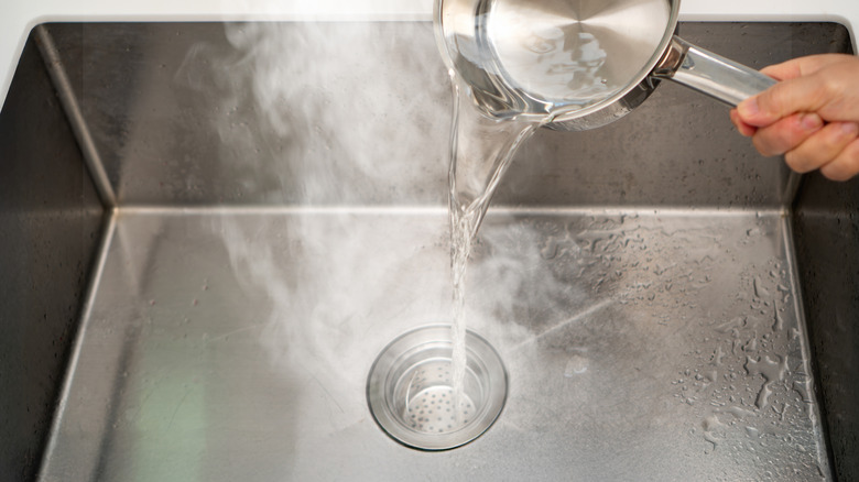 Person pouring a pan of boiling water down a sink drain