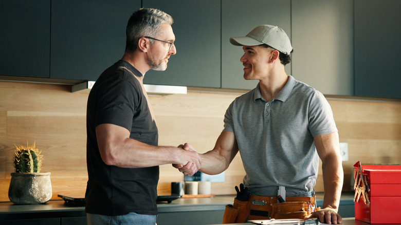 A plumber shaking a homeowner's hand with a red toolbox on the counter