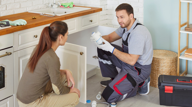 Plumber explaining an issue to a homeowner while dealing with a clogged kitchen drain