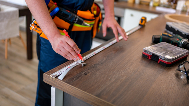 A contractor measures a wood countertop that has a pencil edge