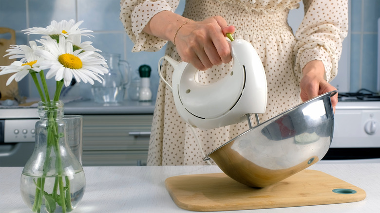 A person using electric mixer to mix something in a metal bowl