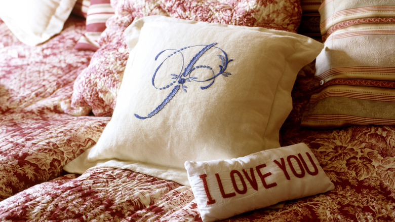 Monogrammed pillows on a red floral quilt.