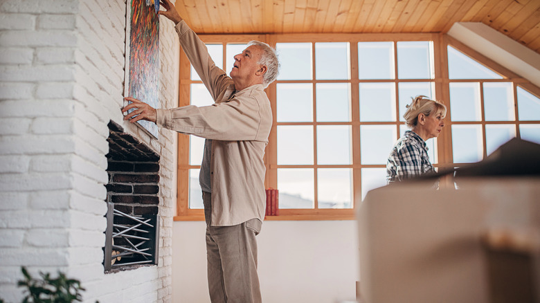 Man hanging a painting above a brick fireplace
