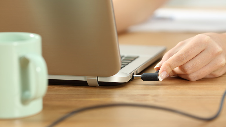 Close up of person plugging laptop into charge cord