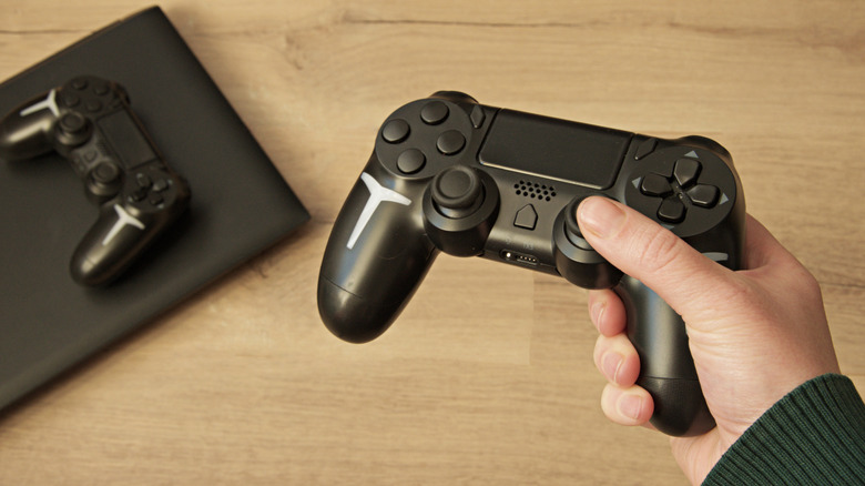 Close up of black gaming console and person holding video game remote