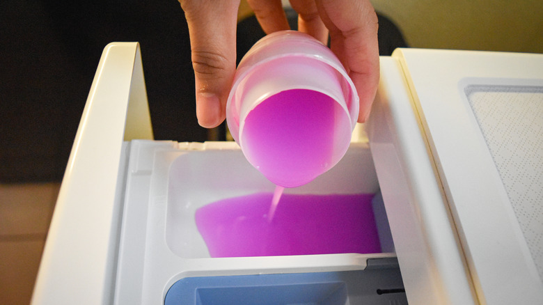 person pouring pink fabric softener into a washing machine