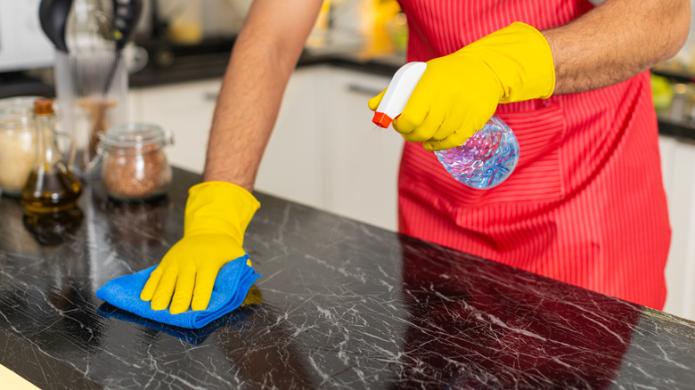 Man wipes kitchen counter with cleaner and microfiber cloth removing grease for hygiene and food safety.