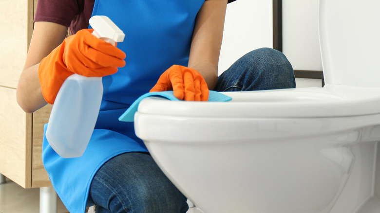 gloved person wiping toilet seat