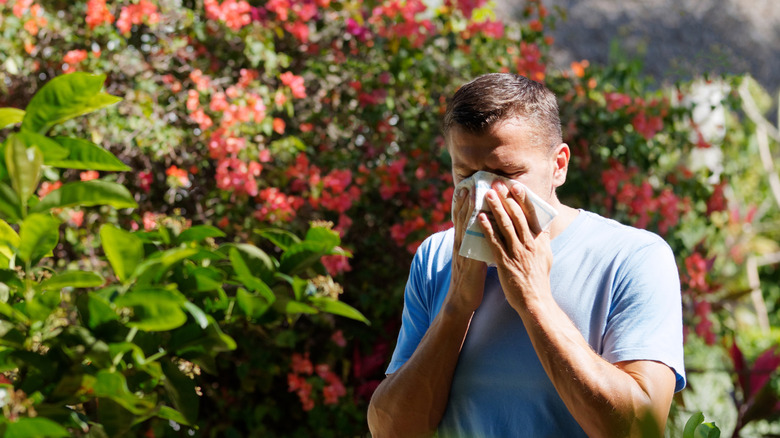 A man holds a small towel to his nose while standing in his backyard.