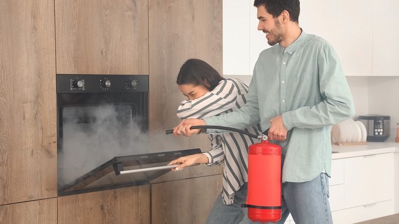 Two people using a fire extinguisher to put out burnt food