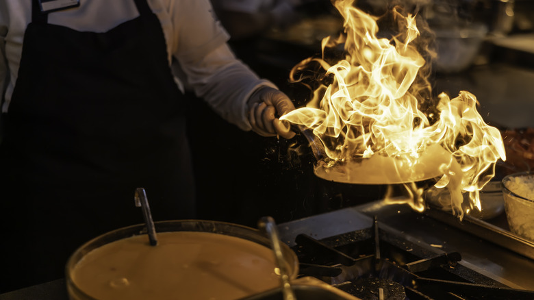 A person holding a burning cooking pan over a stove