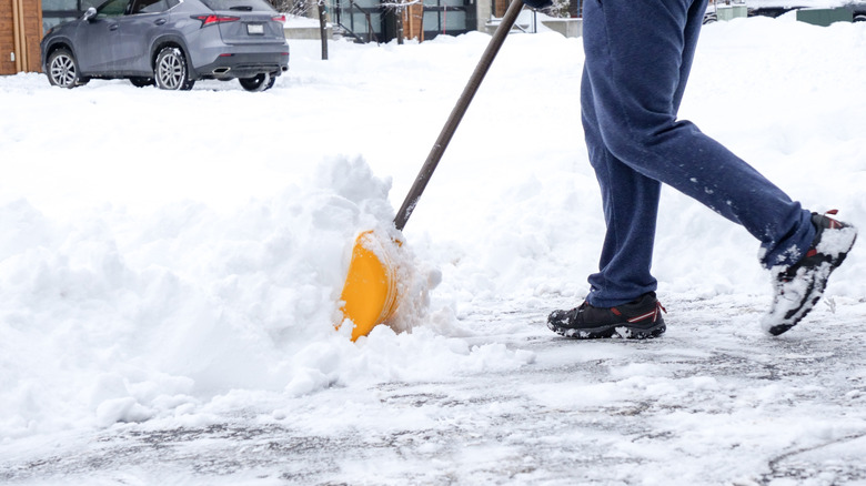 person shoveling snow from their driveway with a car in the background