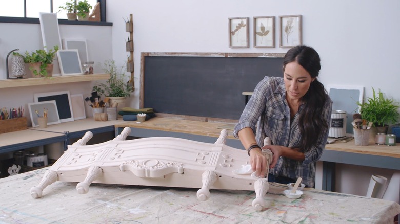 Joanna Gaines painting a decorative bed foot board.