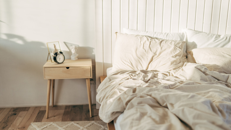 An unmade bed with white sheets and a cream duvet