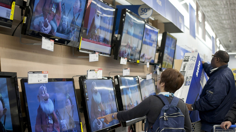 Shoppers looking at TVs mounted to the wall at Walmart