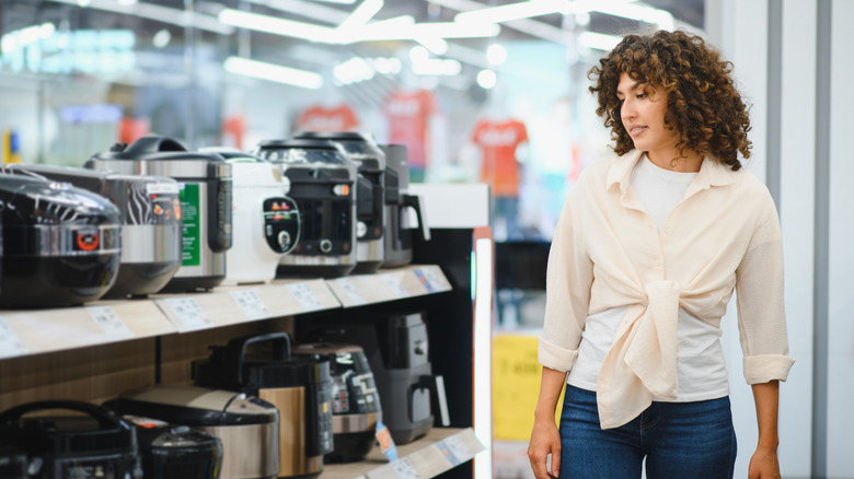 Customer examining a selection of multi cookers in a home appliance store.
