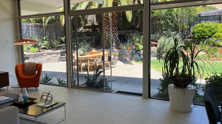 Interior of Eichler home, looking out from living area onto patio through floor-to-ceiling glass windows