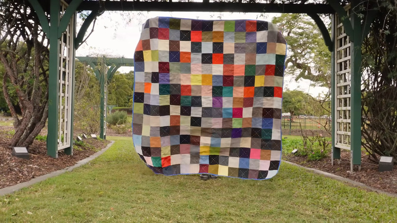 Picnic blanket made of fabric scaps and IKEA bags being held up in a park