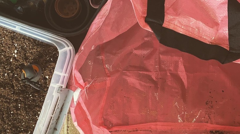 Red plastic IKEA bag being used as a potting mat next to a bin of soil
