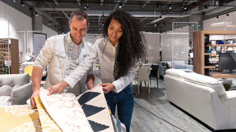 A couple shops together for rugs, looking at various samples.