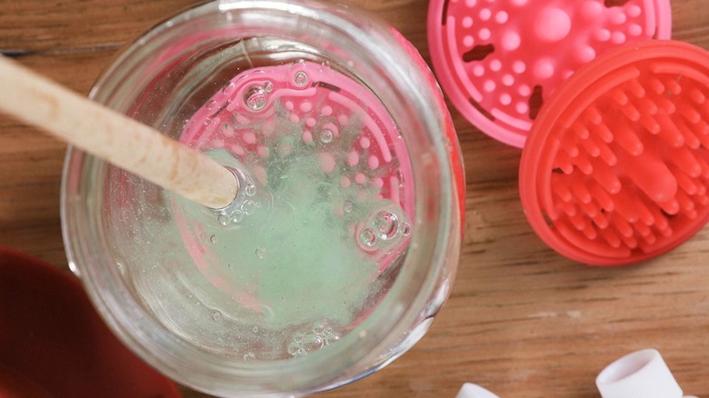 A pink and a red Paint Puck next to a pink paint cup being used to wash a brush in a jar of water