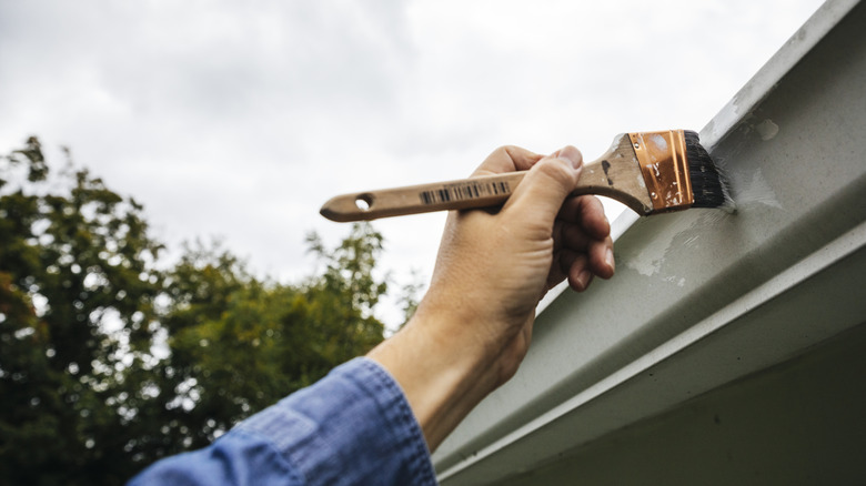 A person painting the fascia on their home with a brush