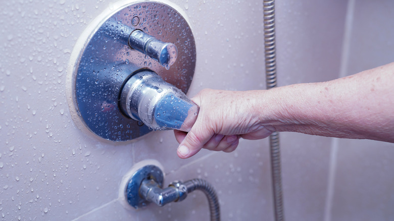 Hand turning on faucet in wet shower.