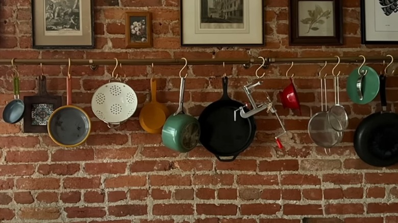 A curtain rod attached to a brick wall with S hooks for hanging cooking pots and utensils