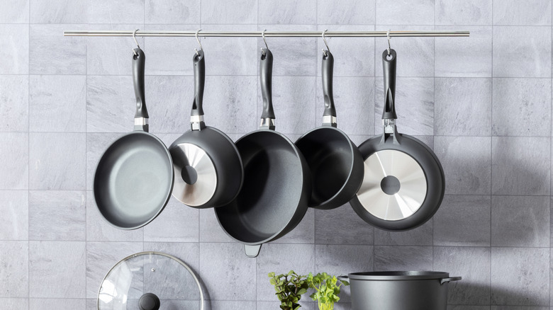 A minimalist kitchen rail is attached to marble tiles, holding a handful of pots and pans