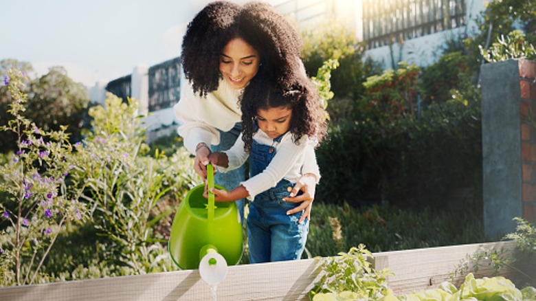 Mother and child using a watering can to water outdoor plants