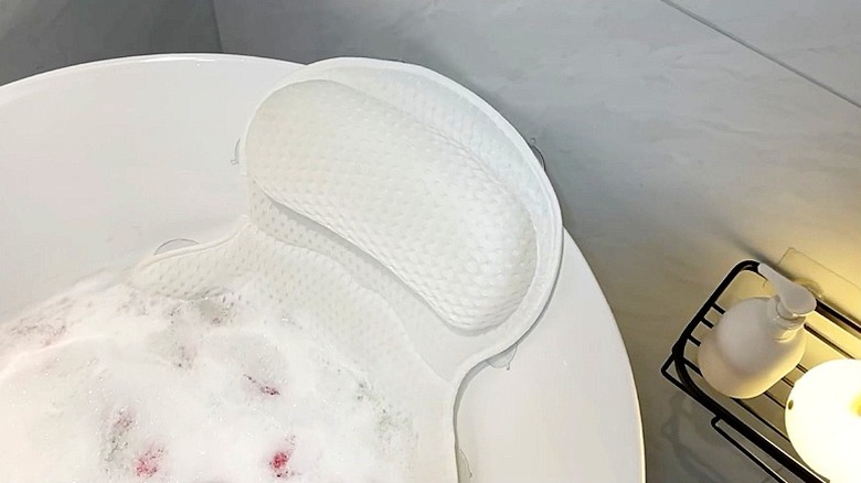A white bath pillow in a white bathtub fulled with bubbles and rose petals