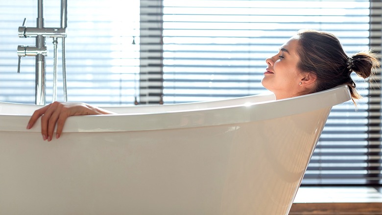A person with their eyes closed smiles while soaking comfortably in a bathtub