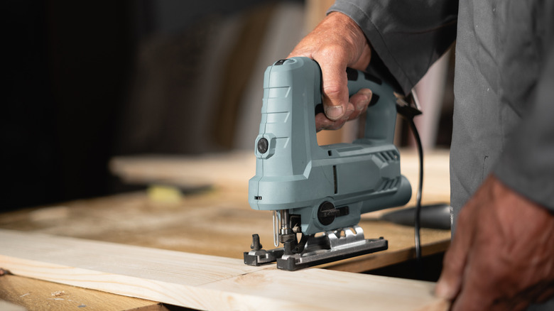 A man cutting wood with a blue-grey jigsaw