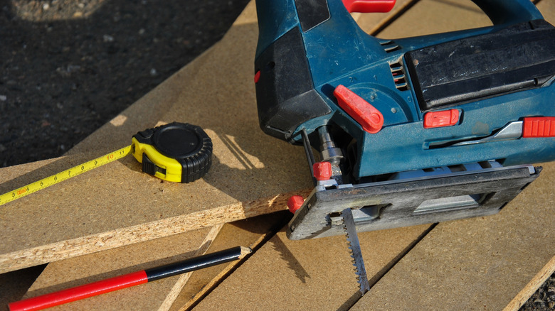 A blue jigsaw, tape measure and pencil on wooden planks